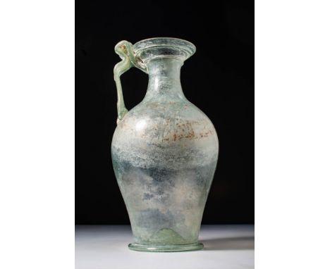 Ca. AD 200 - 300.A translucent light green glass pitcher with a tapered body, prominent shoulder and a flaring rim. It is fit