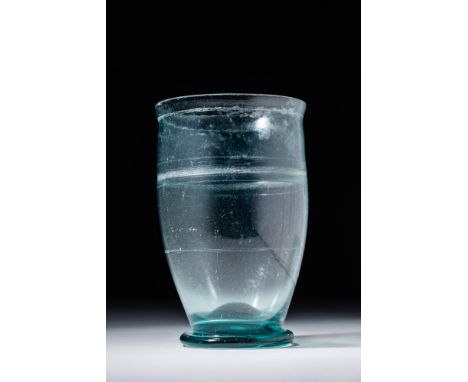 Ca. AD 200 - 300.A clear glass beaker with a tall body that gently tapers towards the bottom. The base is concave, whilst the