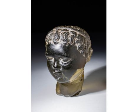 Ca. AD 50 - 150 .A head of a child in translucent dark glass, supported by a short neck. The rounded head is slightly turned 