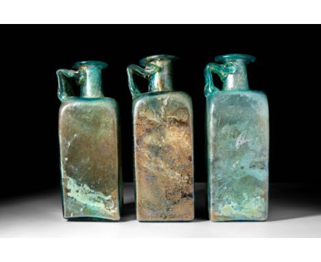 Ca. AD 100 - 400.A collection of three Roman green glass bottles. The bottles have a polygonal shape, a level base and flat s