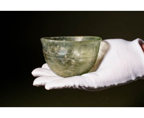 Ca. AD 400 - 600.A green glass facet-cut bowl with a deep rounded form. The base is flattened and cut with two circles and th