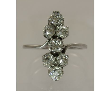 An Art Deco seven stone cluster ring the seven old cut diamonds are claw set in an elegant vertical long configuration with g