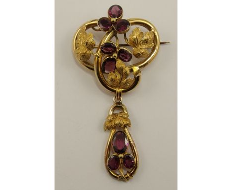 A Victorian garnet brooch the sinuous Art Nouveau form is made in un-hallmarked yellow metal with engraved textured leaves an