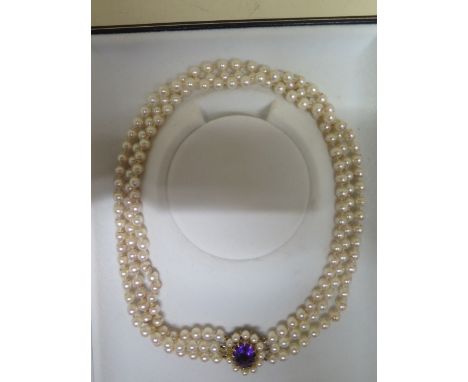 A triple string pearl necklace with a 9ct yellow gold clasp set with central amethyst surrounded with pearls from Cellini, Ca