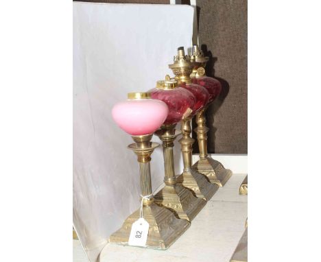 Four brass oil lamp bases with ruby glass reservoirs