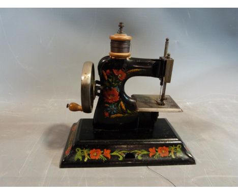 A vintage childs tin plate Casige hand sewing machine with floral detailing and wooden handle and spool. 
H 31.cm. 