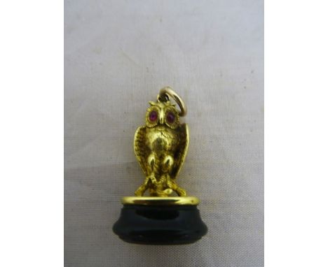 An 18ct unhallmarked model of an owl set with cabochon ruby eyes seated on a perch, uncarved bloodstone seal to base. Height 