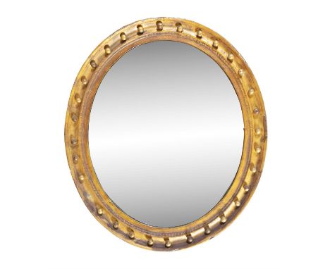AN OVAL GILDED MIRROR, with plain glass plate, bordered with a continuous row of applied spheres.