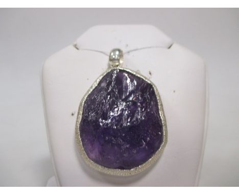 A contemporary amethyst pendant, the oval rough cut amethyst, approx 5cm long x 3.8cm wide in a deep textured rubover mount w