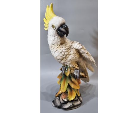 Mid century ceramic probably continental study of a yellow crested Cockatoo perched on a branch amongst foliage on a naturali