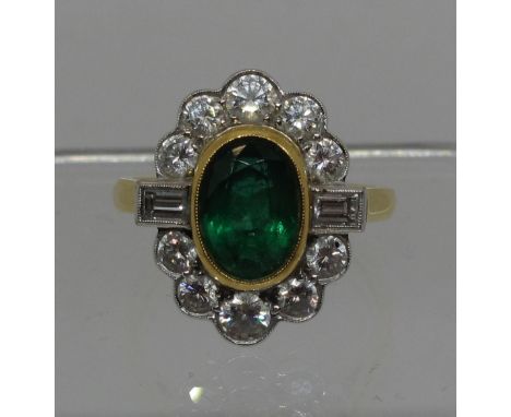 A large emerald and diamond cluster ring.  The oval emerald approx 9x6mm surrounded by ten brilliant cut and two baguette cut