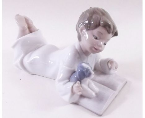 A Lladro Nao figure of a boy lying down reading a book 