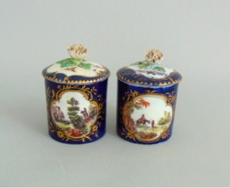 A pair of Derby small pots and covers, cobalt blue ground with gilt border cartouches, each painted with a rural scene to the