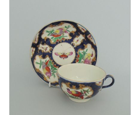 A Worcester tea cup and saucer, painted with exotic birds in gilt cartouches on a blue scale ground, circa 1768-72, fret mark