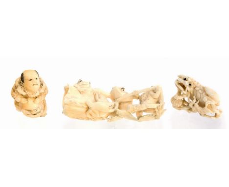 A Japanese carved ivory okimono depicting a frog group pulling a flower, early 20th Century, a carved netsuke of a man claspi