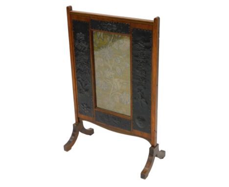 A late 19th/early 20thC oak Arts and Crafts fire screen, applied with hammered brass panels decorated with flowers, stylised 