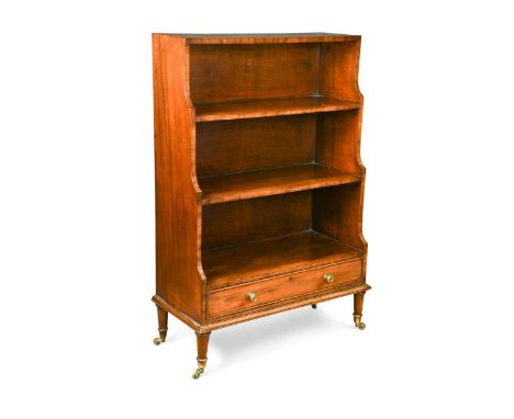 A George III style mahogany waterfall three-tier open bookcase, with long apron drawer, on ring turned feet capped with brass