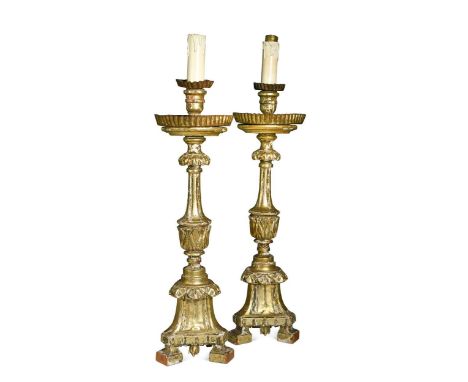 A pair of Italian carved giltwood candlesticks, 18th century and later, the columns decorated with acanthus leaves on triform