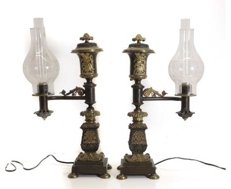 A pair of bronze and brass Argand lamps, 19th century, with an urn shaped finial topping the central support, decorated with 