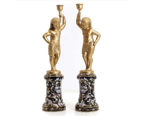 A pair of gilt metal candlesticks, modelled as two Egyptian figures on porcelain plinth bases,38cm high (2)Condition Reportma