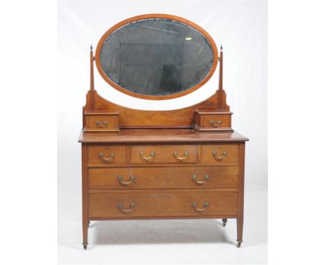 An Edwardian inlaid mahogany dressing table
The oval bevelled mirror enclosed by tapering uprights with brass urn finials, th