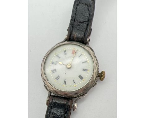 An antique silver cased wristwatch with diamond pattern to case, on a black leather plaited strap. White enamel face with bla
