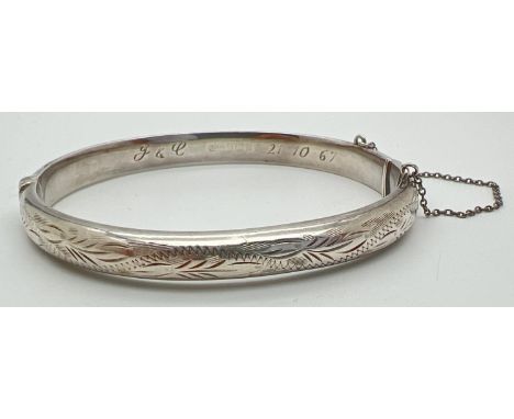 A vintage silver bangle with half floral engraved detail and safety chain. Inscription to inside of bangle "J &amp; C 21.10.6