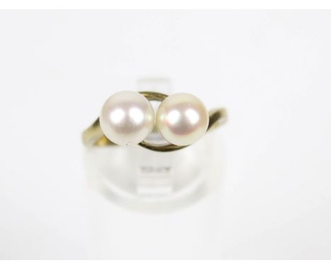 A Continental cultured-pearl two-stone cross-over ring. The 6.4mm diameter beads set within a cross-over scroll head on a D-s