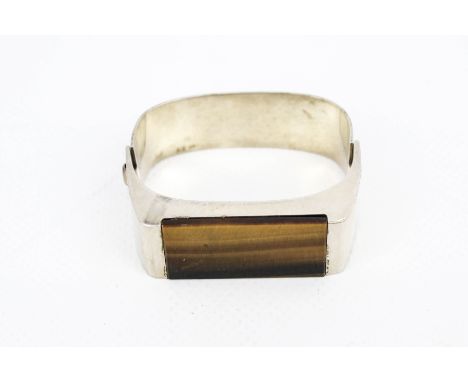 A white metal and tiger's-eye quartz broad bangle. In two articulated sections, the front of the 'oblong' bangle loosely set 