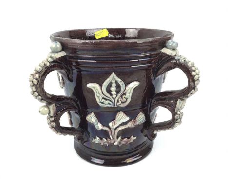 Castle Hedingham pottery four handled loving cup with applied 1650 and floral decoration on brown ground, 18cm high
