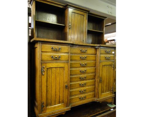 A stylised Art Nouveau oak dresser, the top having open shelves and cupboard, the base fitted with 7 short central music draw