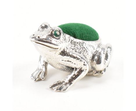 A sterling silver frog pin cushion. The frog having a green velvet pin cushion to the back with round cut green stones set to