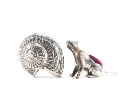 A silver cat pin cushion together with a silver shell shaped vesta case. The pin cushion depicting a slender cat scratching i