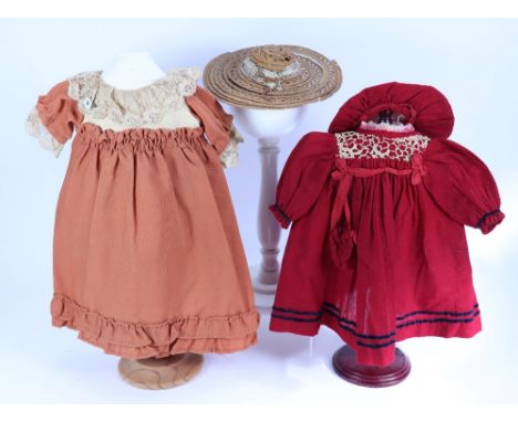 Two dolls dresses, circa 1910, including a red wool dress with long sleeves, lace to bodice, black velvet trim, bag and match