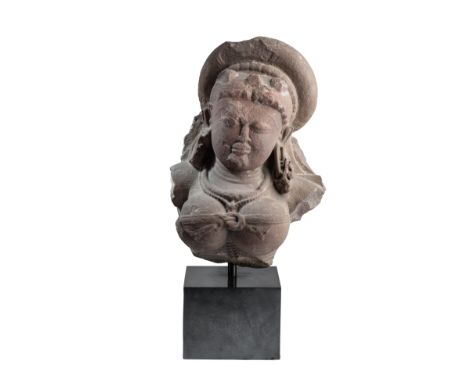 A PINK SANDSTONE FRAGMENTARY BUST OF DURGA, CENTRAL INDIA, CIRCA 10TH CENTURY her hair gathered in a wide bun, wearing earrin