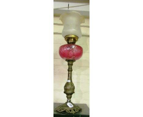 A brass oil lamp with red reservoir and frosted shade