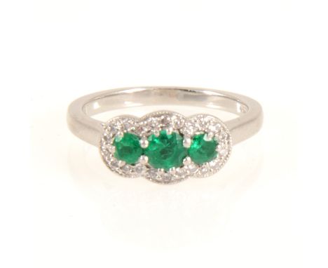 An emerald and diamond cluster ring, three round faceted emeralds surrounded by twenty-two brilliant cut diamonds in a platin