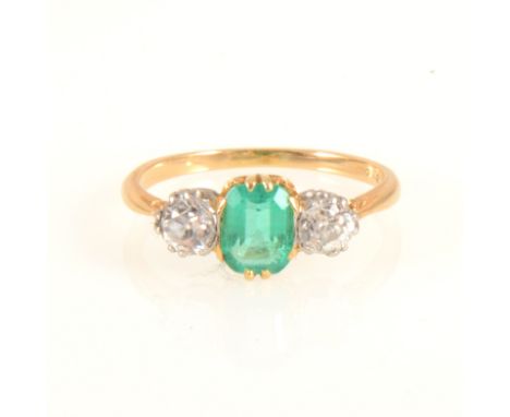 An emerald and diamond three stone ring, the rectangular step cut emerald 7mm x 5mm, claw set with a old brilliant cut diamon