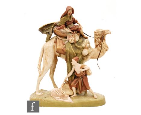 An early 20th Century Royal Dux figural group modelled as an Arab riding a camel with a servant at his side carrying bags, mo