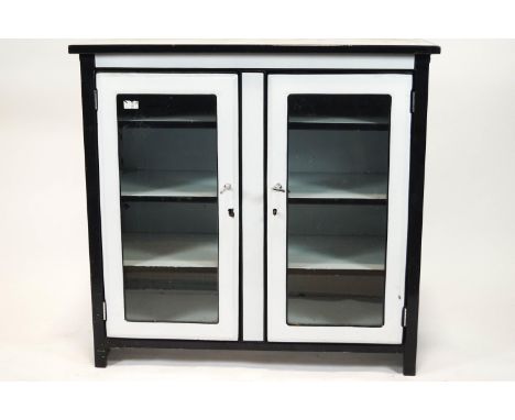 A 1950's white enamel cabinet with black enamel banding, the glazed doors enclosing three hanging shelves, 92cm high x 96cm w