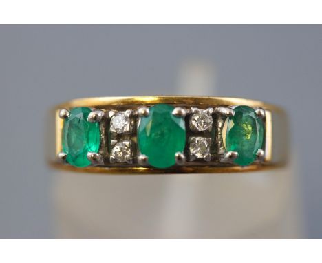 A yellow and white metal half hoop ring. Set with three oval faceted cut emeralds interspaced with diamond pairs. Hallmarked 