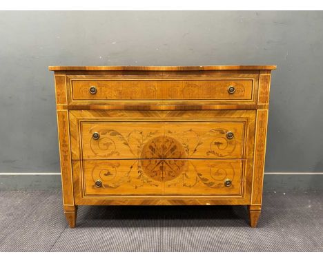 A reproduction commode in the Louis XVI style, decorated with arabesque design around central motif incorporating crossed fla