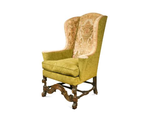 A carved walnut-framed wingback armchair, 17th century, raised on scroll and lion paw feet united by a scrollwork apron and t