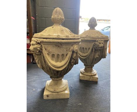 A pair of composite stone neoclassical style gate post finials in the form of lidded urns, decorated with lion masks and drap