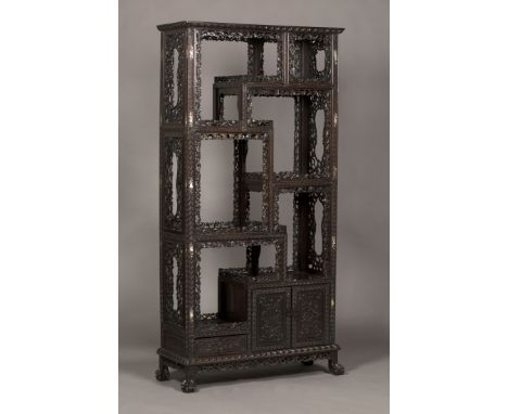 A Chinese hardwood display shelf, late 19th Century, with an arrangement of asymmetrical shelves above a cupboard and drawer,