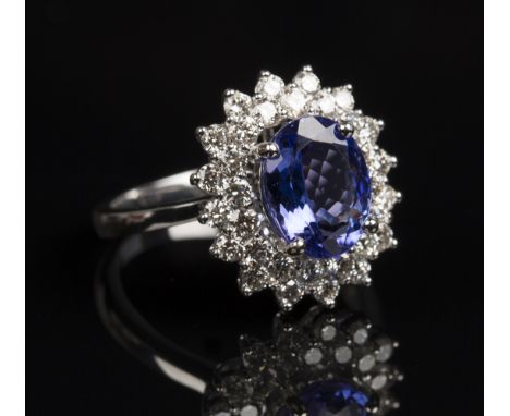 A white gold, tanzanite and diamond oval cluster ring, claw set with the oval cut tanzanite within a two row surround of circ