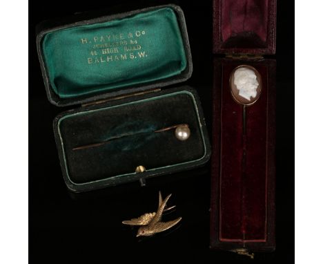 A gold brooch, designed as a bird in flight with a cabochon red gem set eye, detailed '15ct', an oval shell cameo stick pin, 
