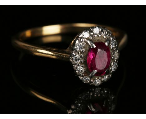 A gold, platinum, ruby and diamond oval cluster ring, claw set with the oval cut ruby within a surround of circular cut diamo