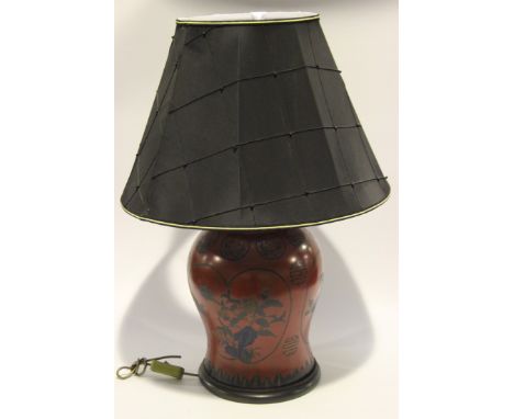 A 20th Century Chinese red lacquered table lamp of baluster form, the black silk shade above the body decorated with reserves