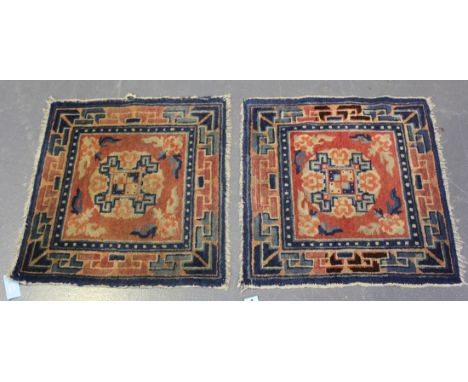 A pair of Chinese mats, early 20th Century, each pink field with a circular medallion, within a running angular scroll border